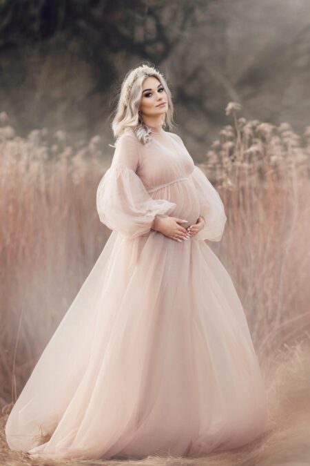 pregnant woman wearing latte tulle maternity gown with long sleeves in natural field
