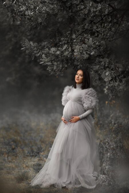 pregnant woman in light gray tulle maternity dress with voluminous sleeves in apple orchard